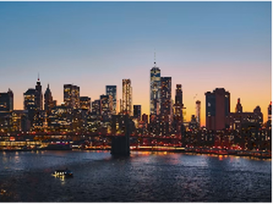 The Manhattan skyline at dusk seen across the water, its towers lit against a fading sky.