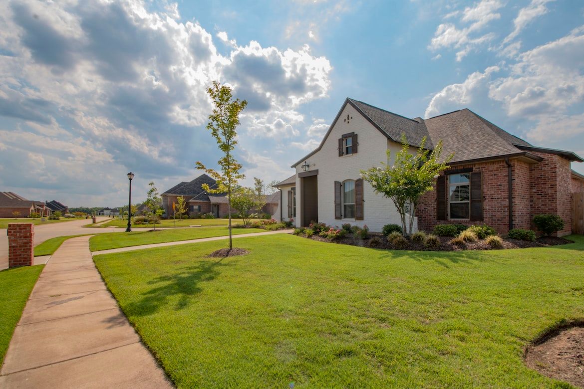 A brick suburban house with a green lawn and a curving sidewalk under a wide, open sky.